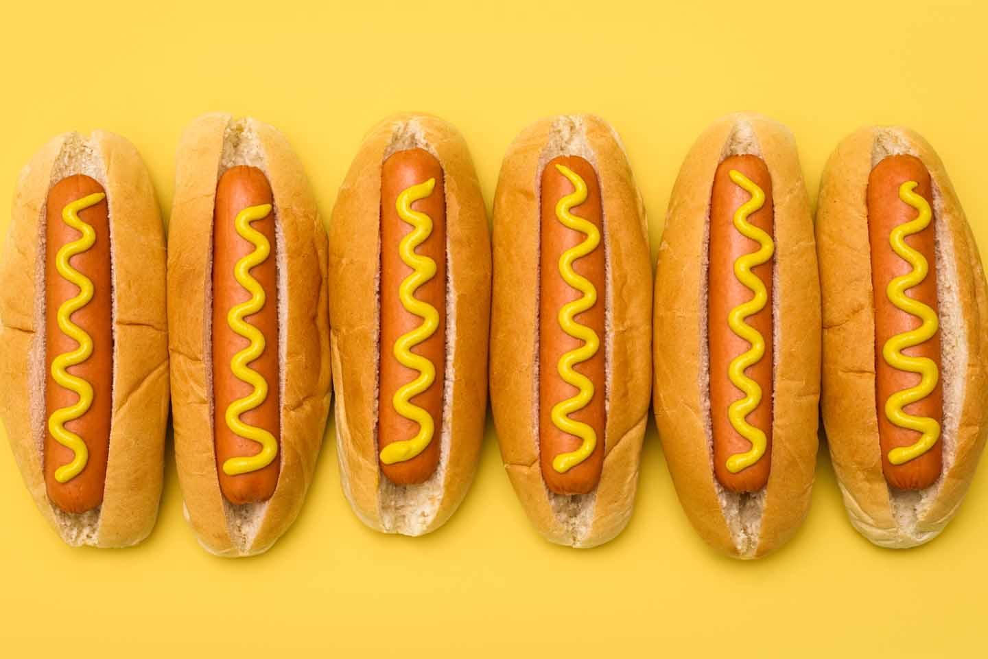 Hotdogs: Würstchen im Brötchen mit Senf darauf liegen nebeneinander.