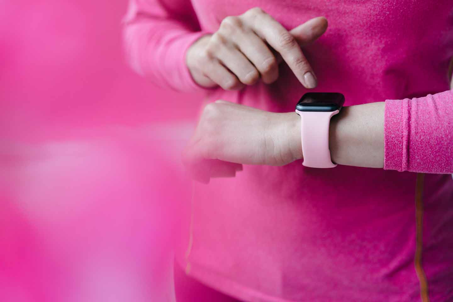 Eine Frau mit einem pinkfarbenen Pulli schaut auf eine rosa Armbanduhr.