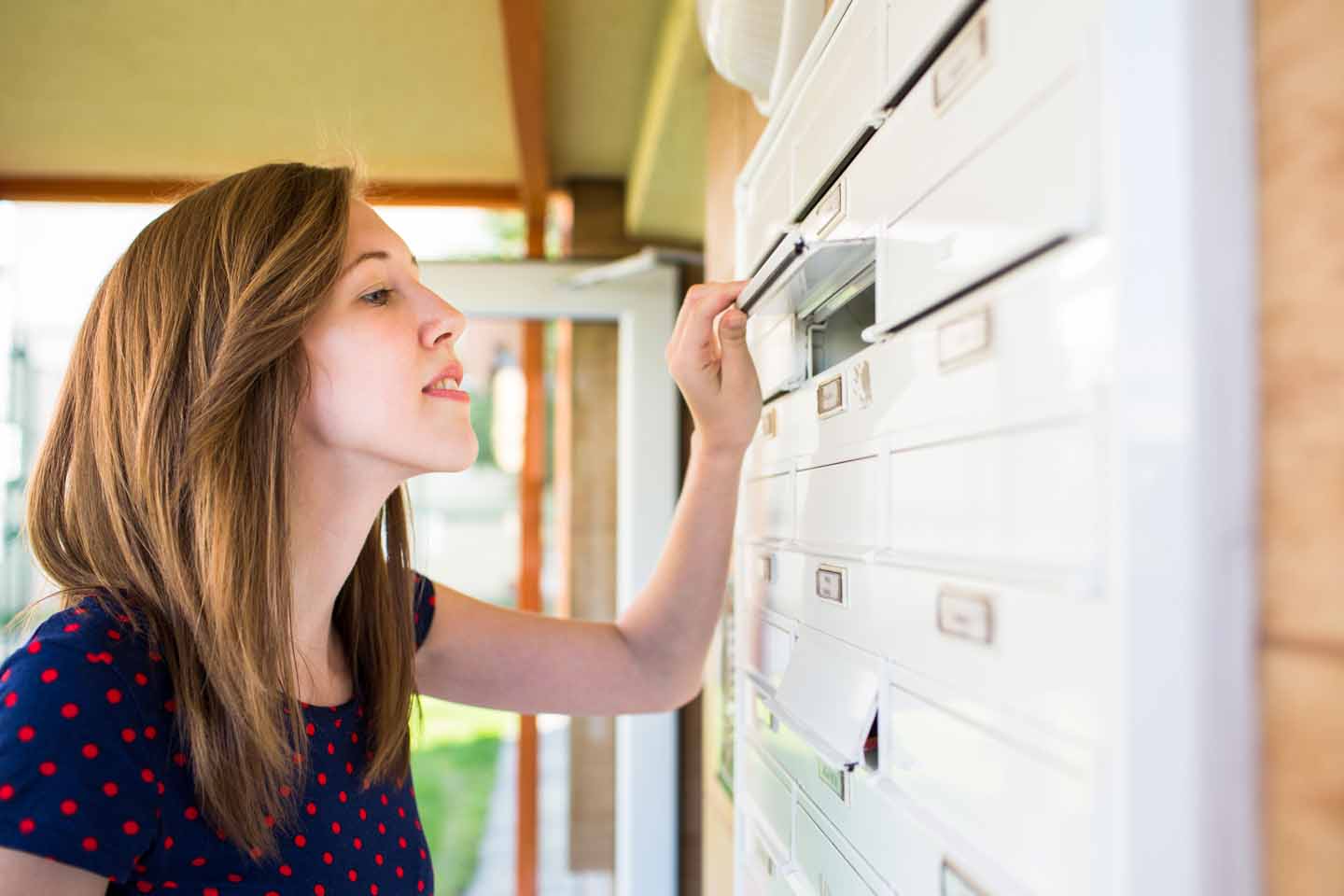 Eine Frau schaut in den geöffneten Briefkasten.