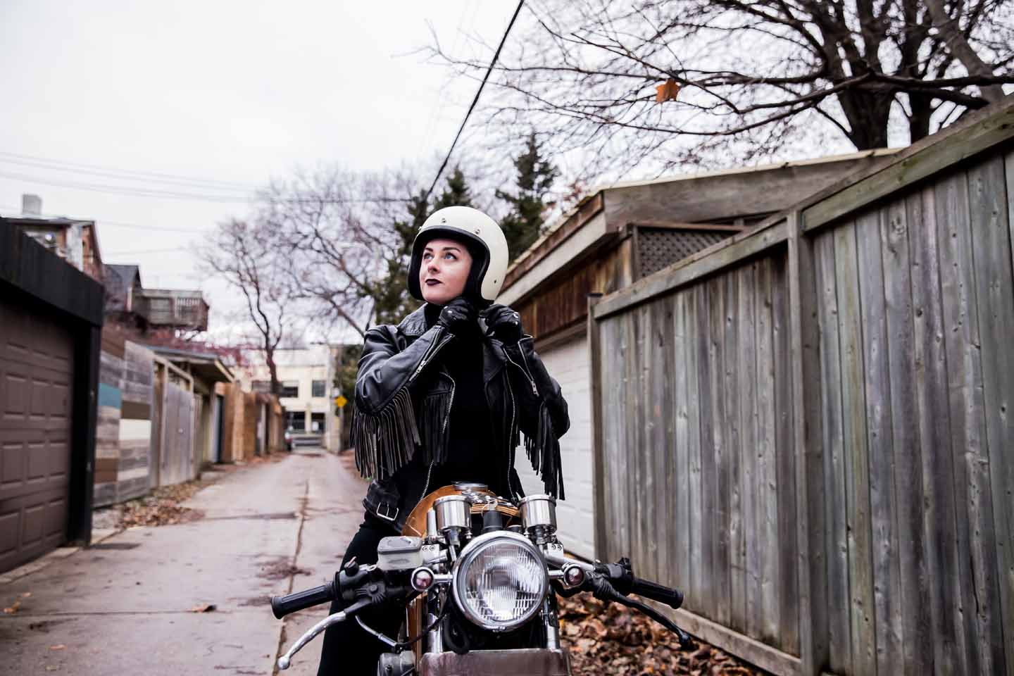 Eine Motorradfahrerin setzt in einem Garagenhof einen Helm auf.