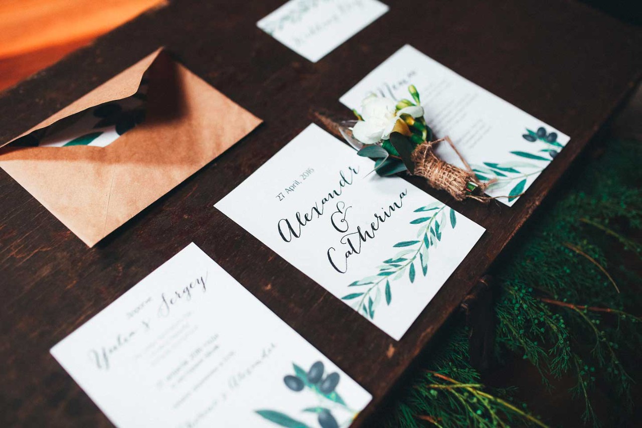 Auf einem Holzbrett liegen ein Briefumschlag und Einladungs- sowie eine Menuekarte für eine Hochzeit.