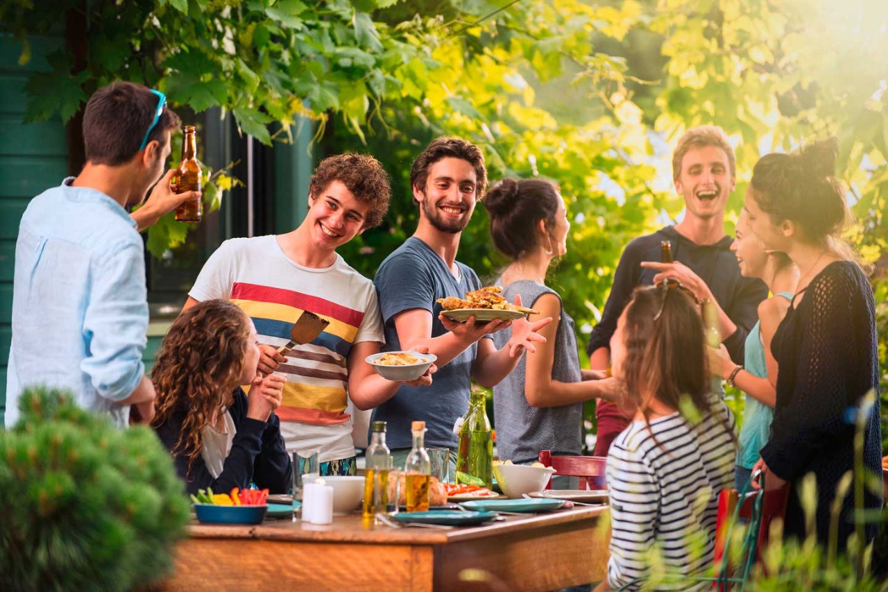 Junge Leute feiern freudig auf einer Terrasse, trinken, essen und unterhalten sich.