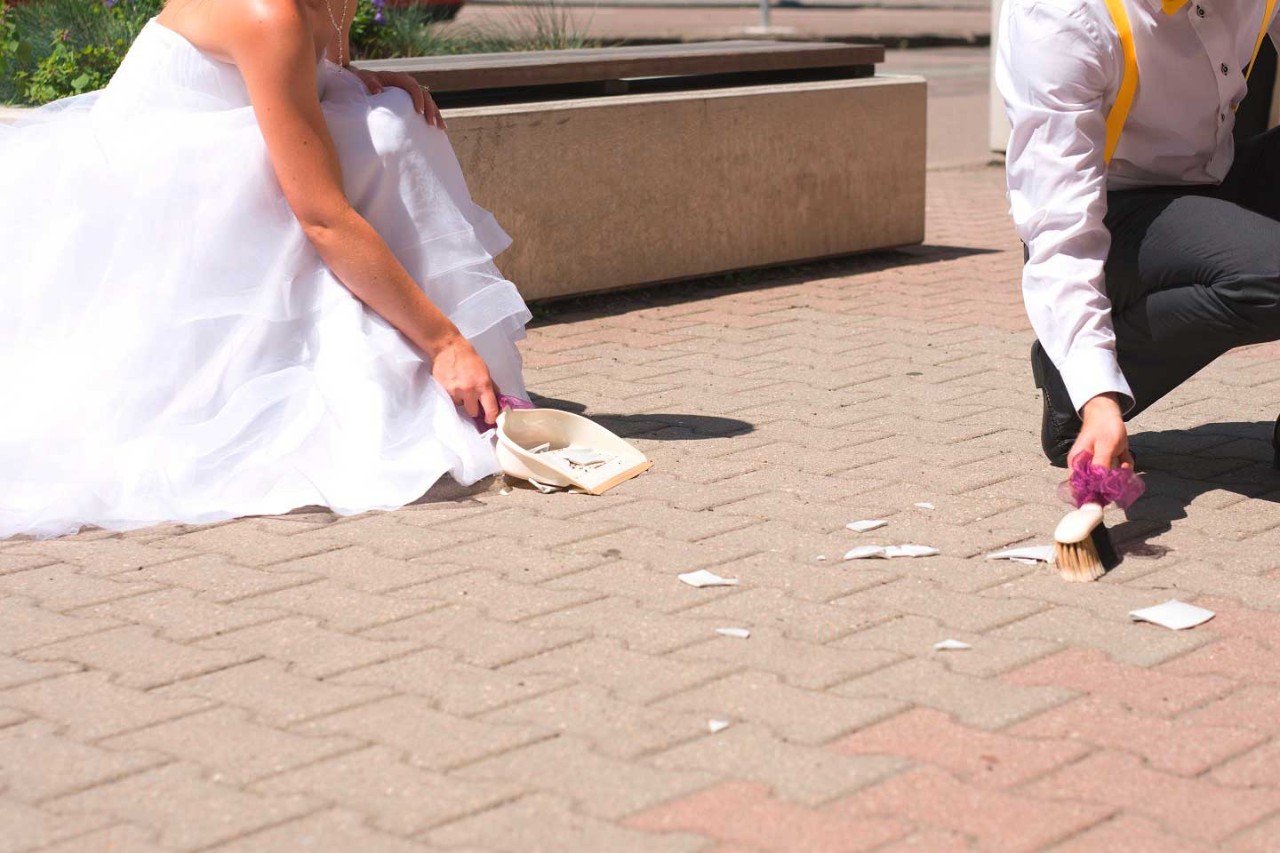 Braut und Bräutigam kehren mit Besen und Schaufel gemeinsam Scherben auf.