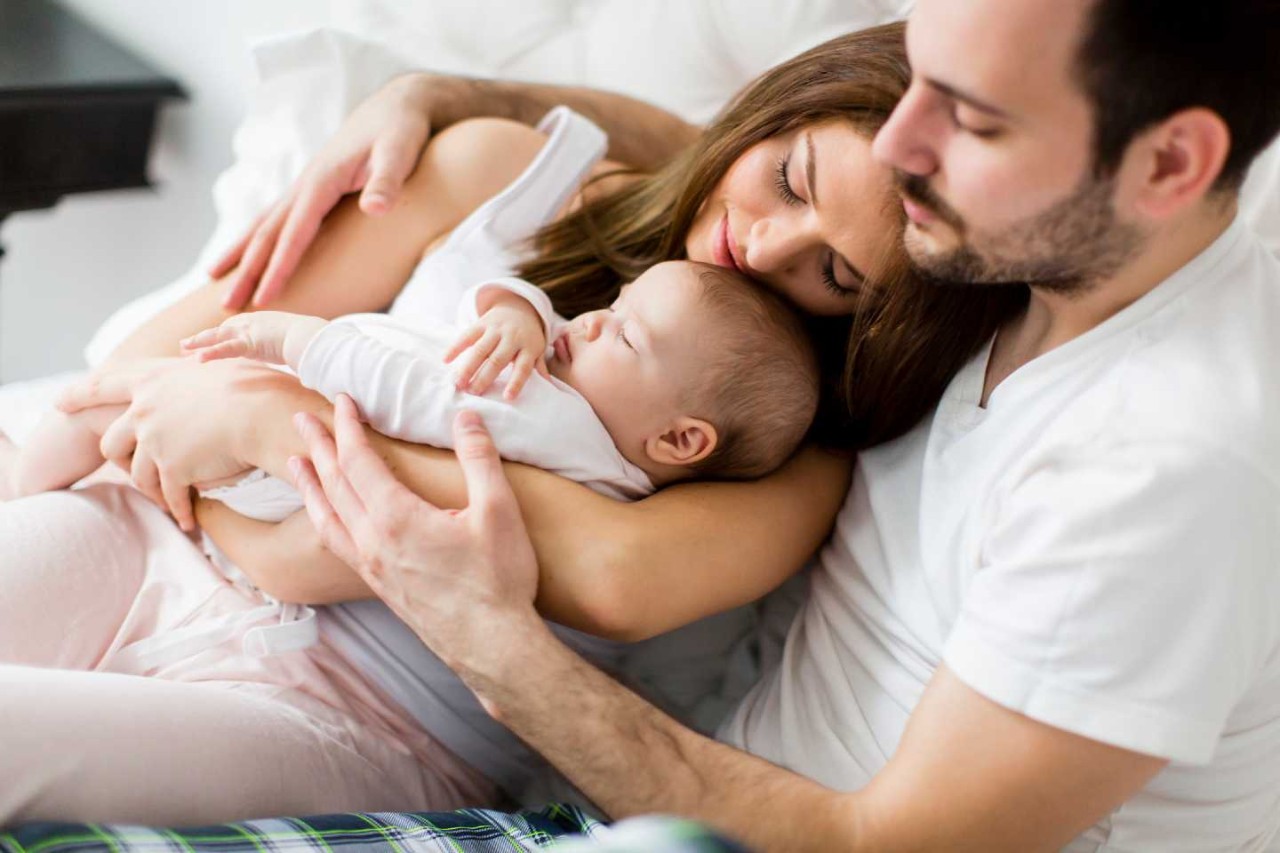 Frisch gebackene Eltern schmusen im Schlafanzug mit dem Neugeborenen auf dem Arm.