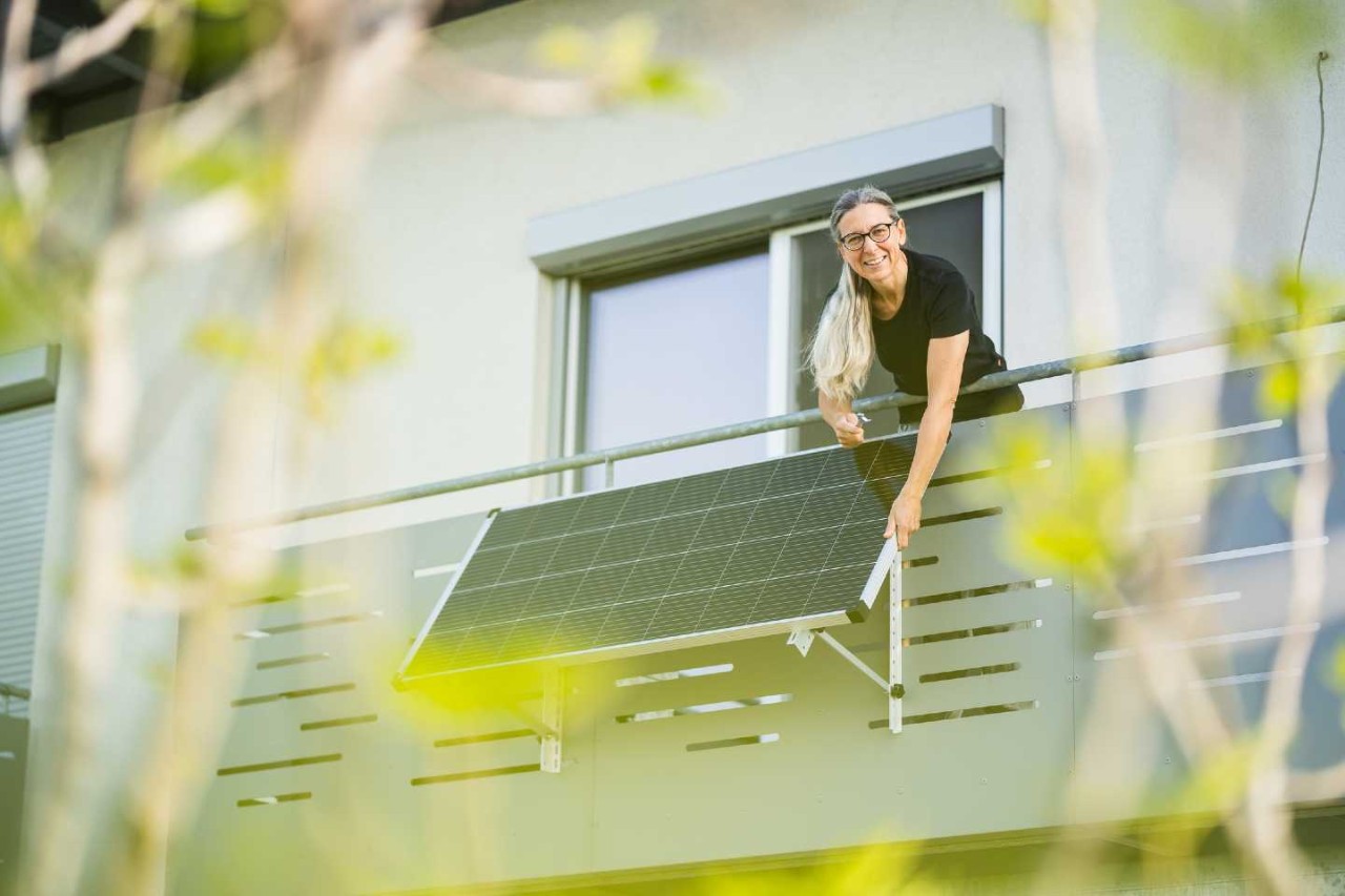 Eine Frau installiert ein Solarmodul am Balkon.
