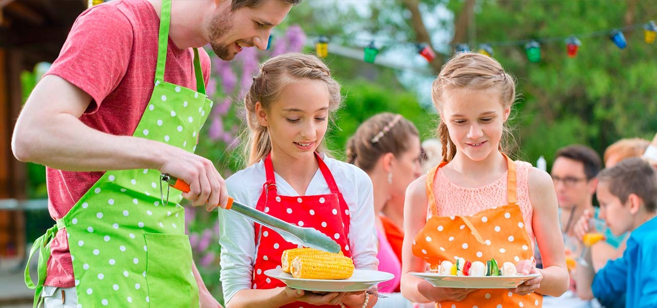 Richtig grillen – Kinder mit Grillschürzen beim Grillen mit einer Aufsichtsperson